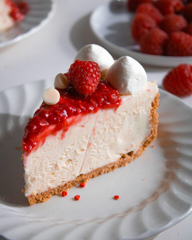 Slice of no-bake gelatin free white chocolate raspberry cheesecake on white plate