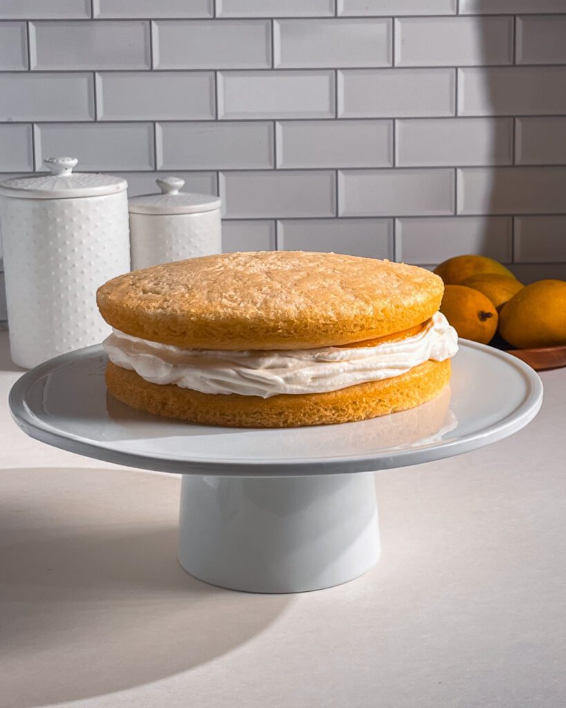 Layering whipped cream and mango filling between cake layers