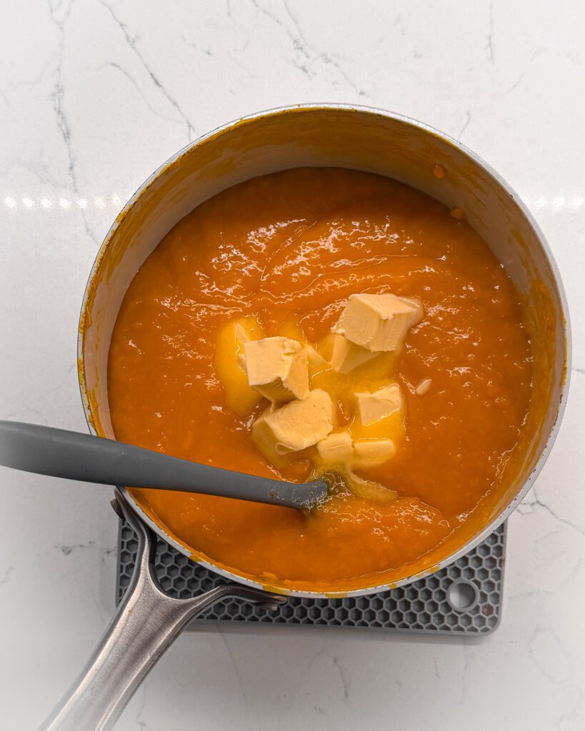 Mixing butter to mango curd cooking in saucepan