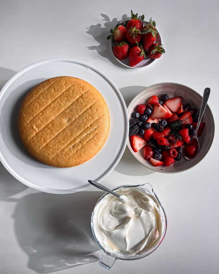 Assembling an eggless berry cream cake with fresh seasonal berries.
