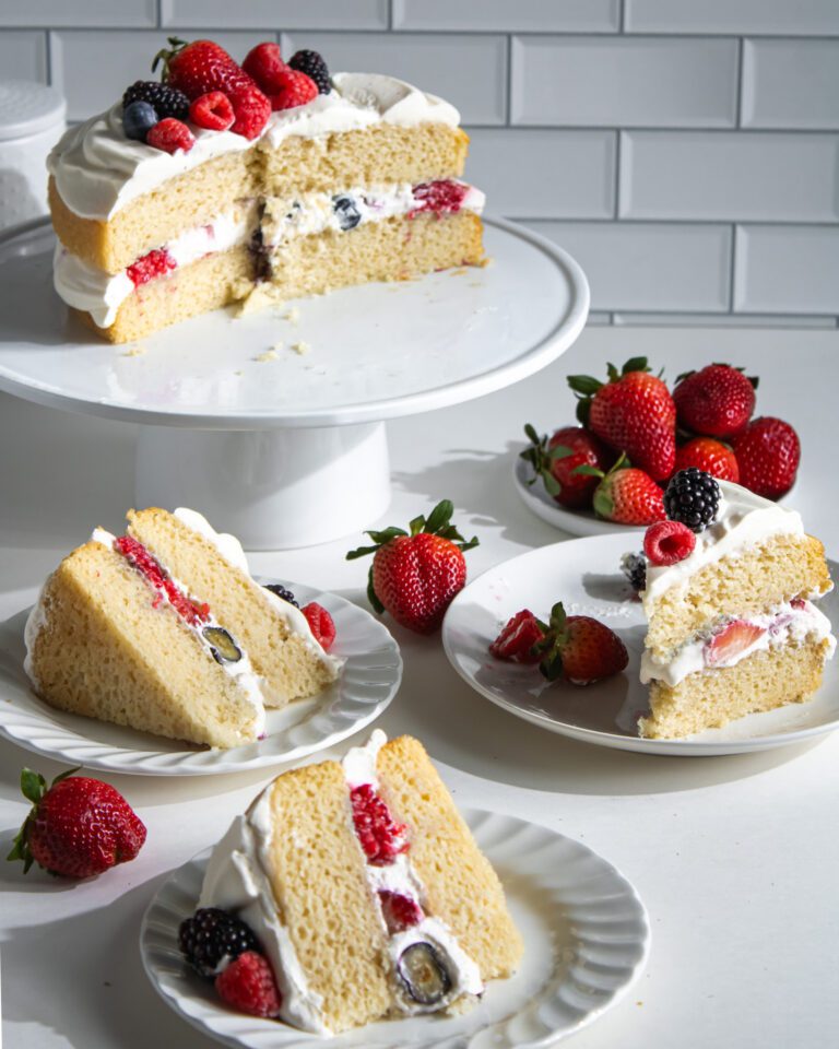 Close-up of a slice of eggless berry cream cake showing layers of vanilla sponge, whipped cream, and berries.