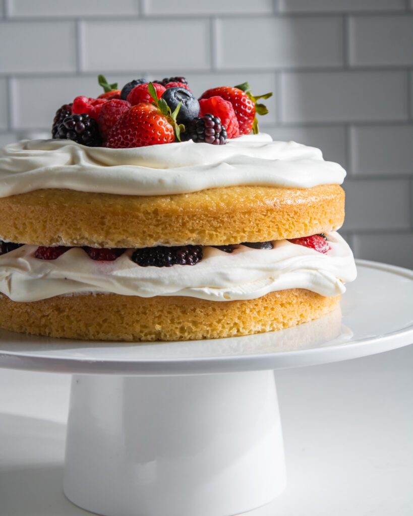 Decorating a berry cream cake with fresh strawberries and blueberries.