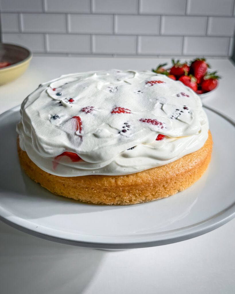 Frosting a homemade berry cream cake with smooth whipped cream.