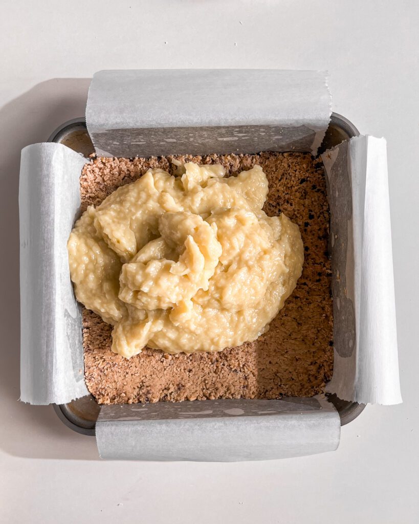 Pouring homemade coconut custard over the chilled biscuit crust.