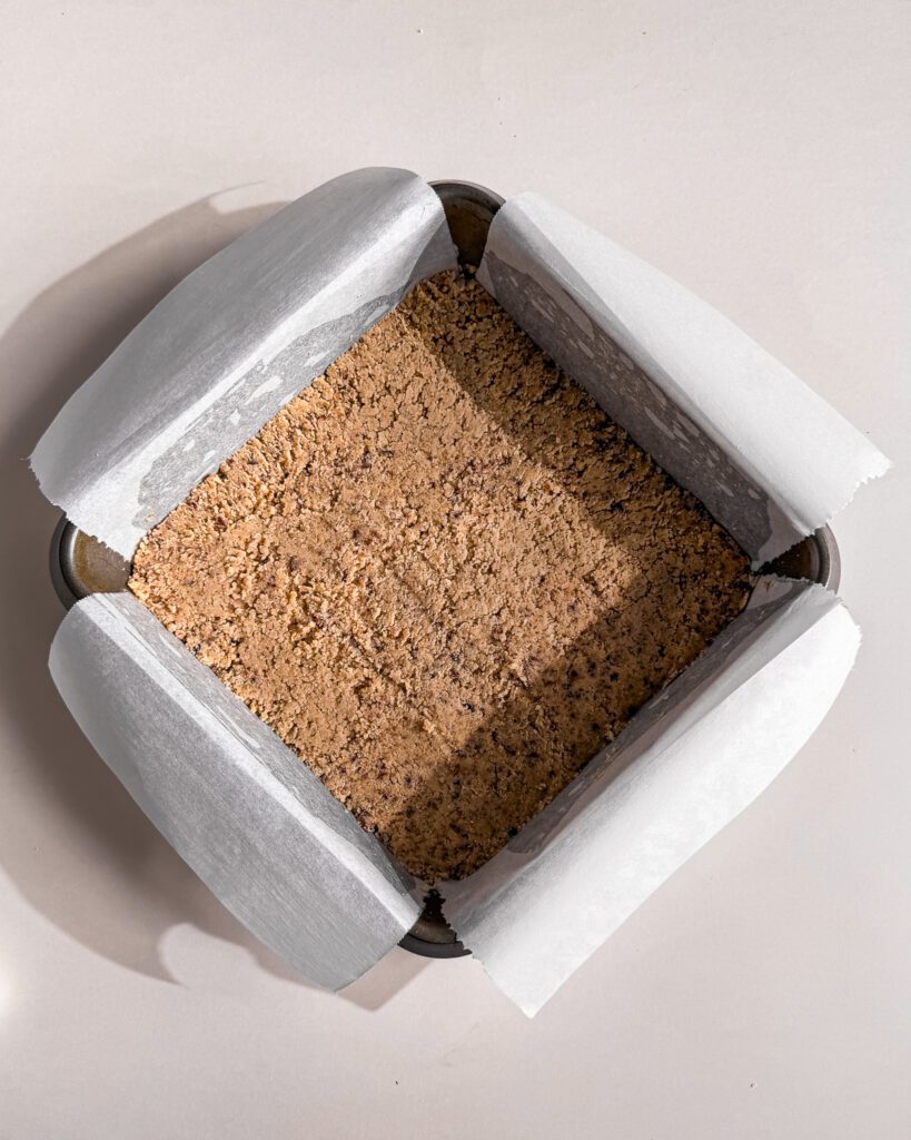 Pressing the biscuit crumb mixture into a square baking pan.