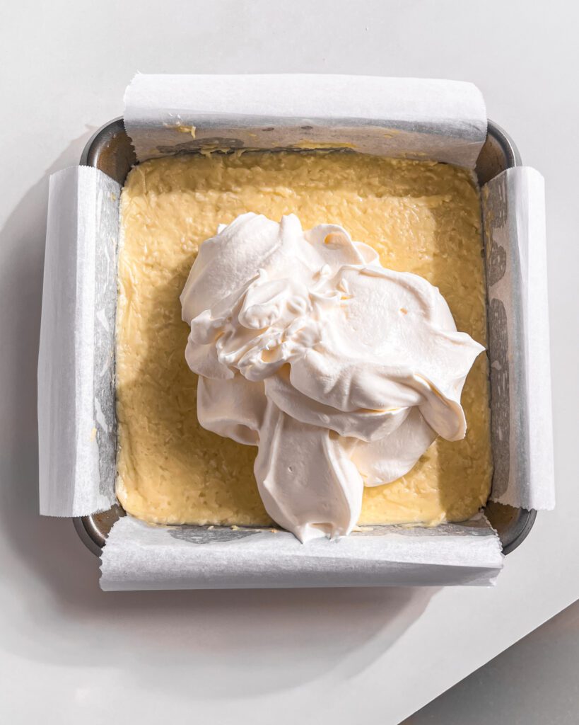 Spreading whipped cream over the chilled coconut custard layer.