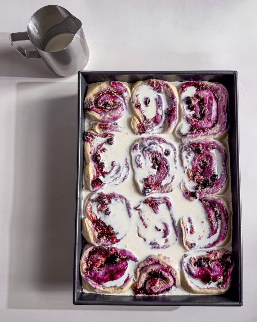 Pouring whipping cream over blueberry cinnamon rolls