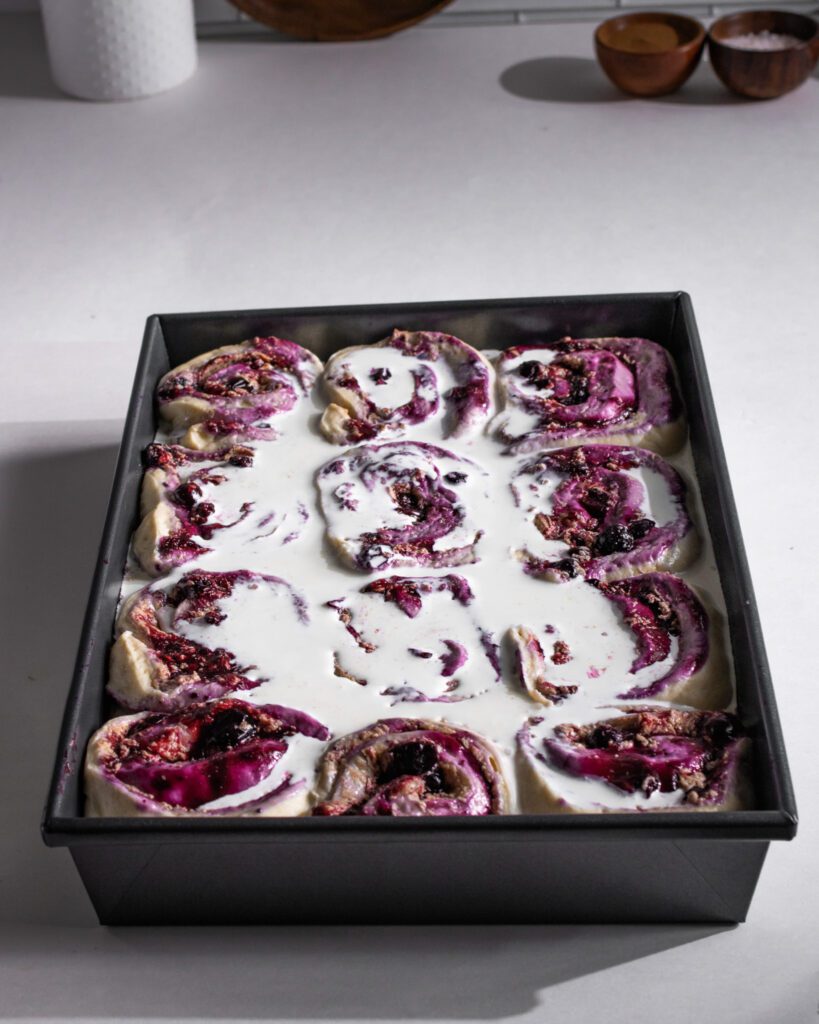 Pouring whipping cream over blueberry cinnamon rolls before baking