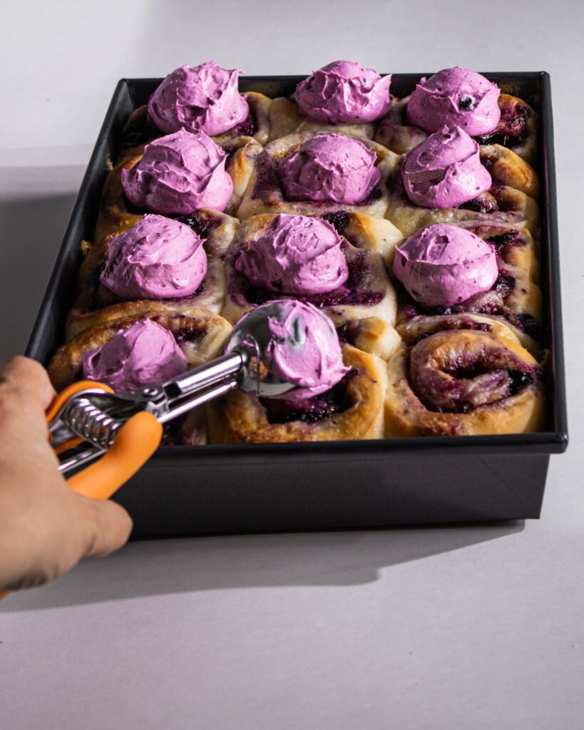 Spreading blueberry frosting over warm cinnamon rolls