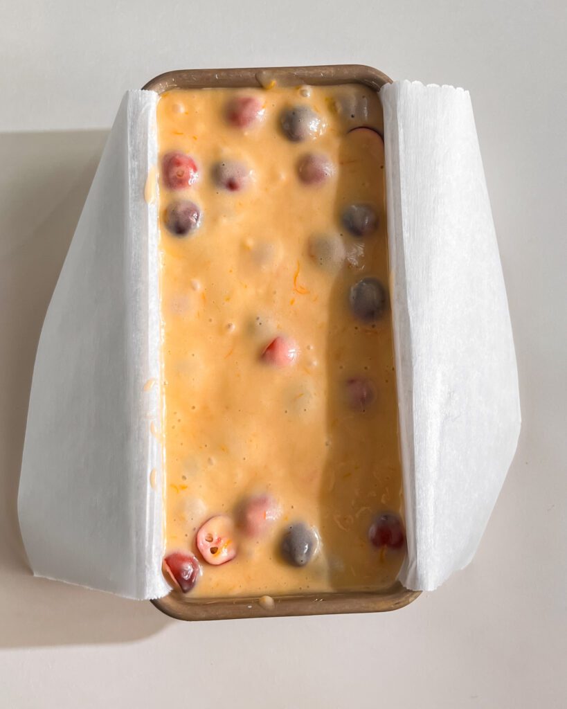 Orange cranberry cake batter spread evenly in a parchment-lined loaf pan