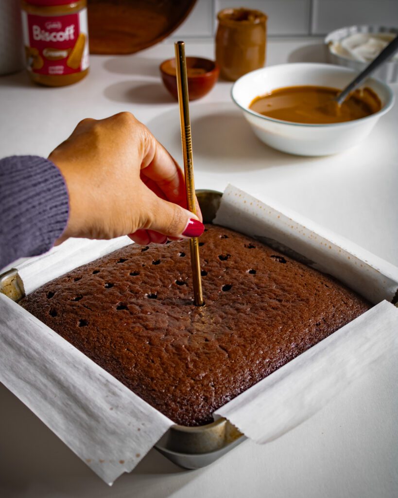Holes poked across a chocolate sponge cake before adding melted Biscoff spread